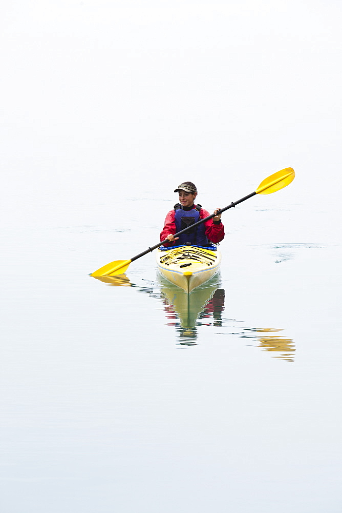 Female sea kayaker paddling pristine waters of Muir Inlet overcast sky in distance, Glacier Bay National Park, Alaska