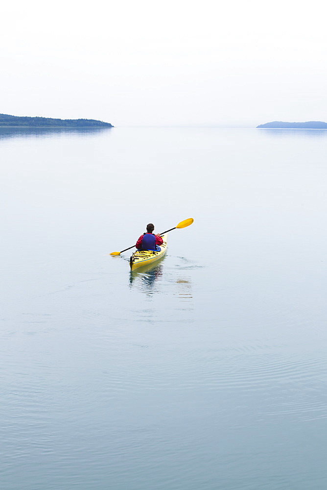 Female sea kayaker paddling pristine waters of Muir Inlet overcast sky in distance, Glacier Bay National Park, Alaska