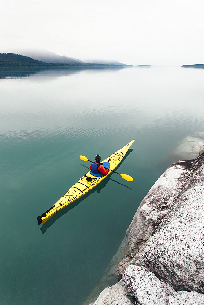 Female sea kayaker paddling pristine waters of Muir Inlet overcast sky in distance, Glacier Bay National Park, Alaska