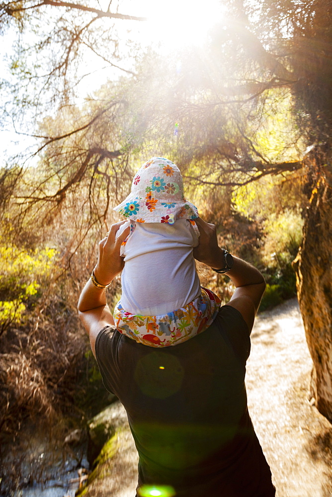 Mother giving her baby girl a piggyback ride on nature path by a thermal pool, Rotorua, North Island, New Zealand