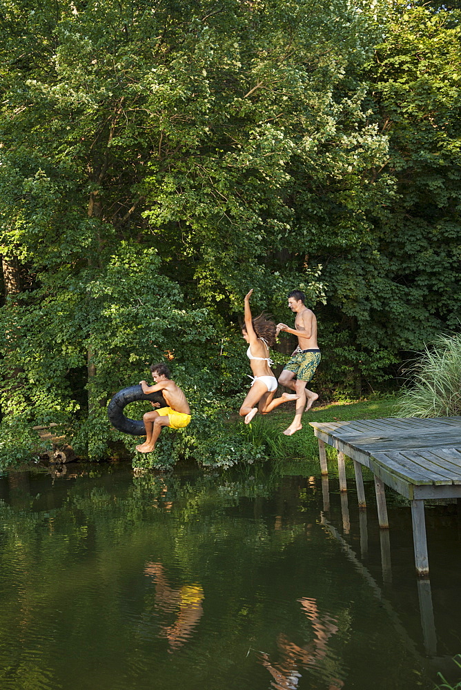 Three young boys jumping from the jetty into a still pool of water, Maryland, USA