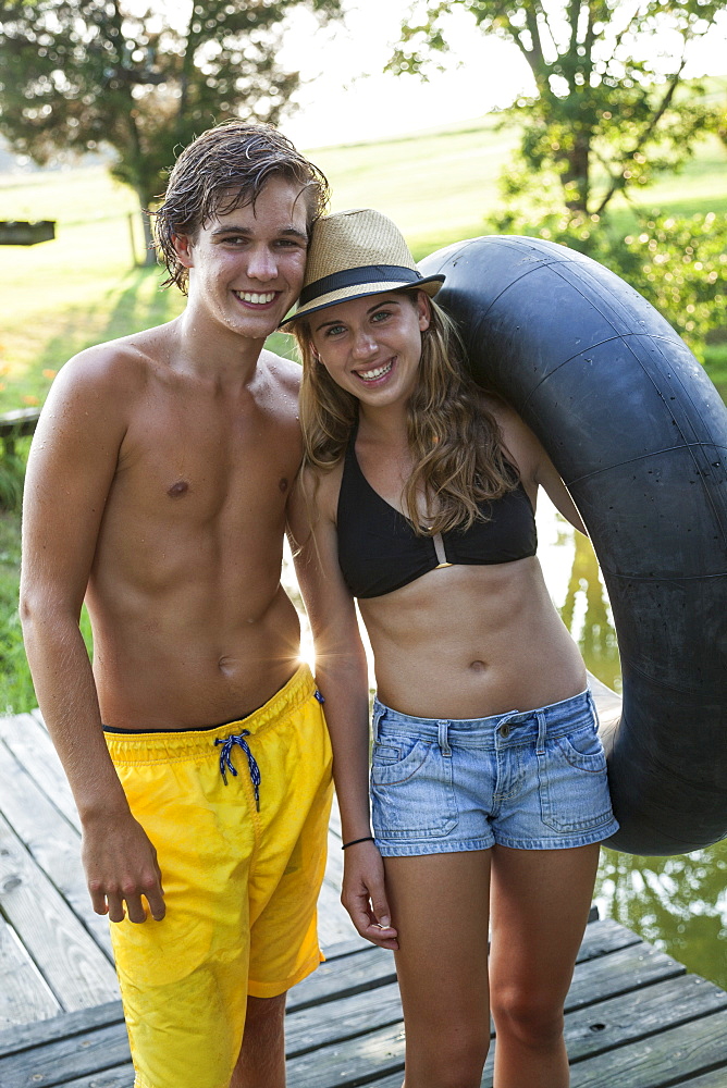 Young teenagers, boy and girl on a jetty by a water pool, holding a swim float, Maryland, USA