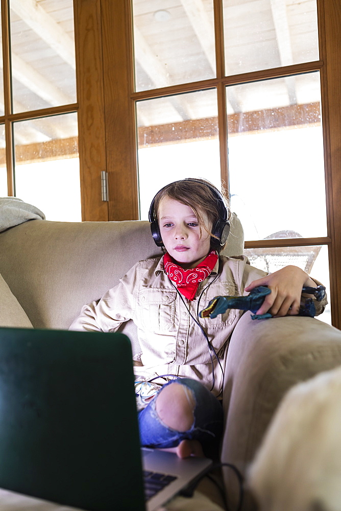 Young boy wearing safari outfit and headphones watching a movie on laptop