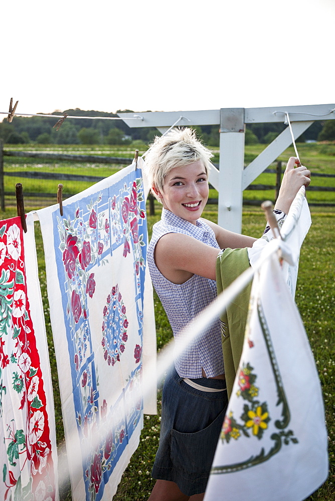 A young girl, teenager, hanging out the washing, pegging patterns fabric sheets to a washing line, Maryland, USA