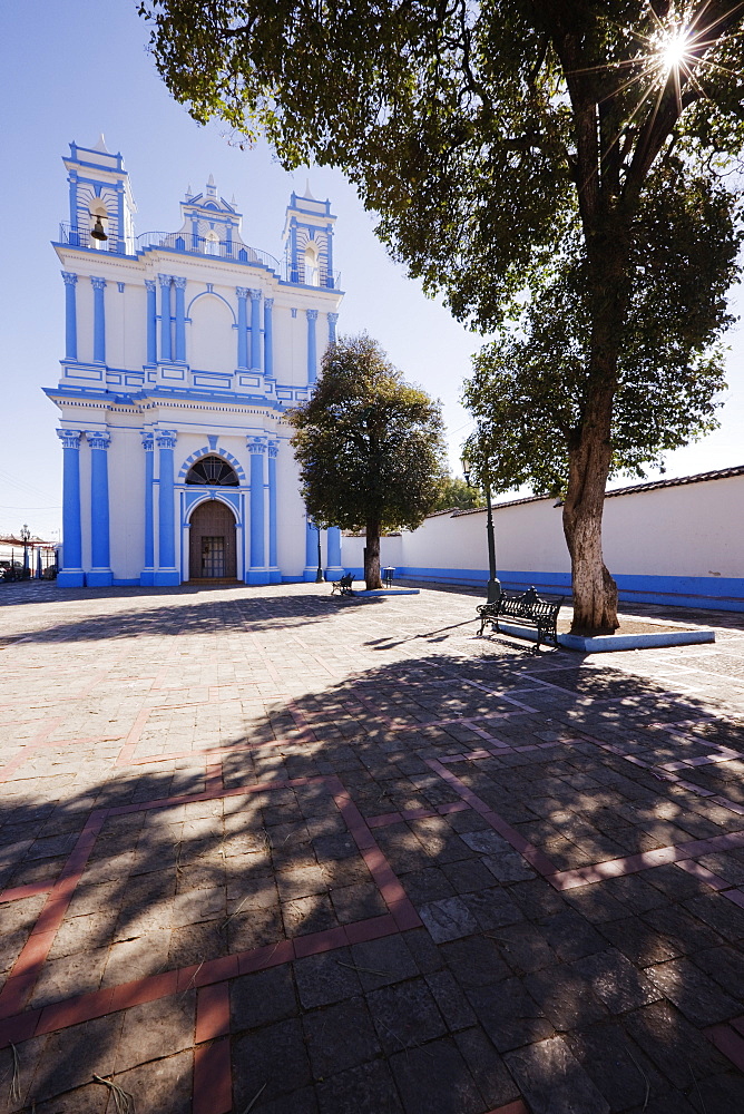 Church in a town square and a shady bench under a tree