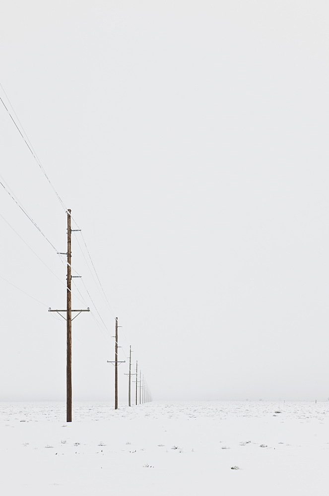 Power lines in snowy wintry landscape with grey sky