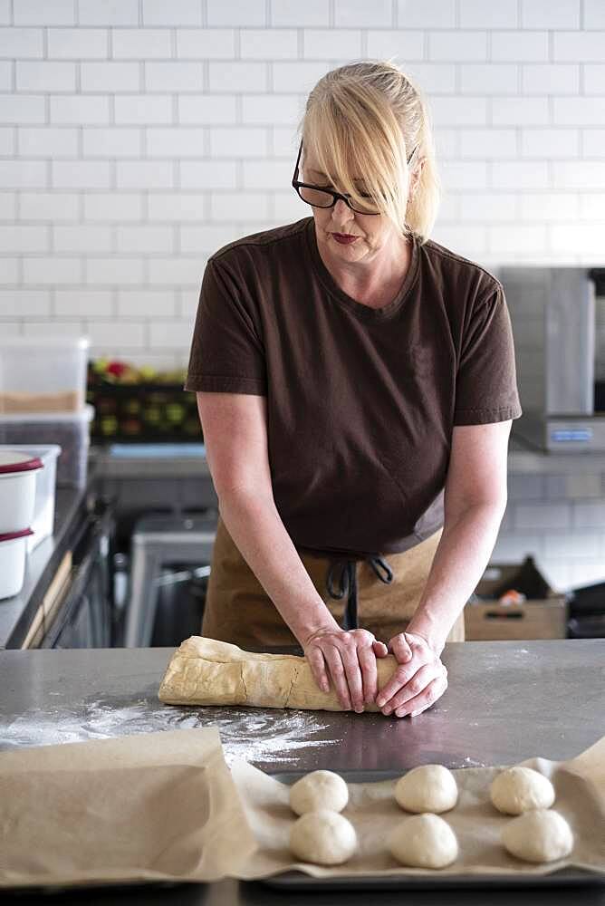 Woman in brown apron standing in a cafe kitchen, mixing baking danish pastry dough