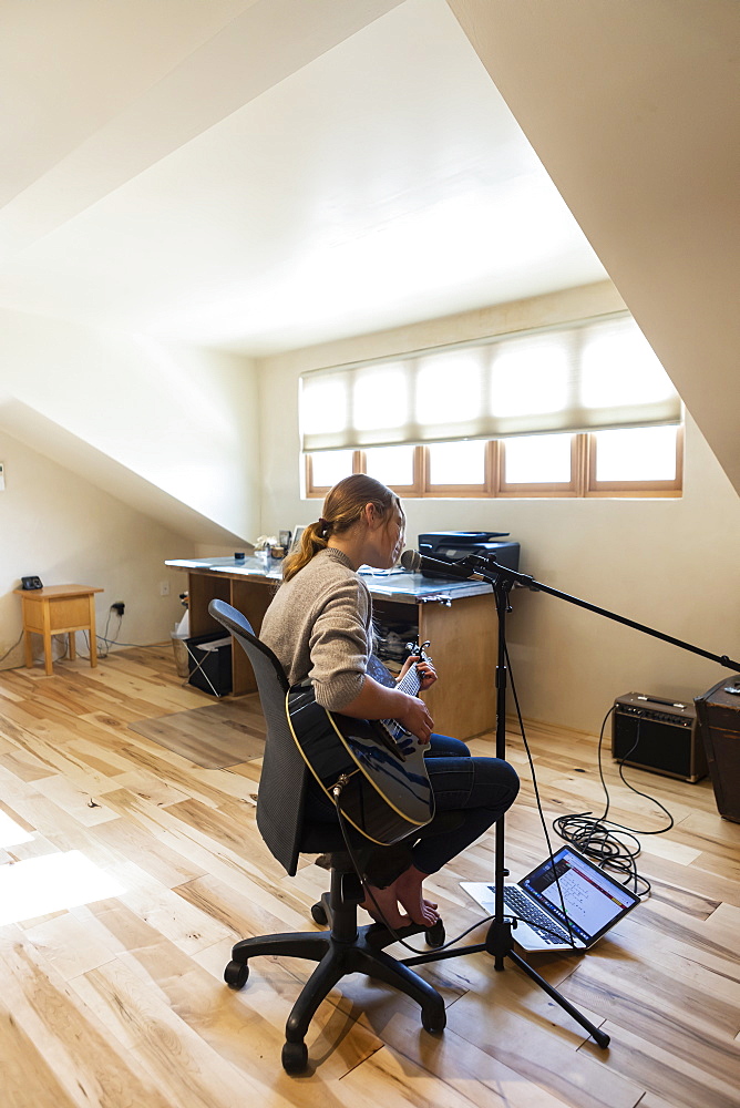 Fourteen year old teenage girl playing her guitar and singing at home in loft space