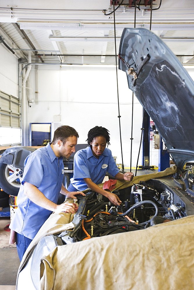 Male and female mechanics talk as they look at engine in auto repair shop