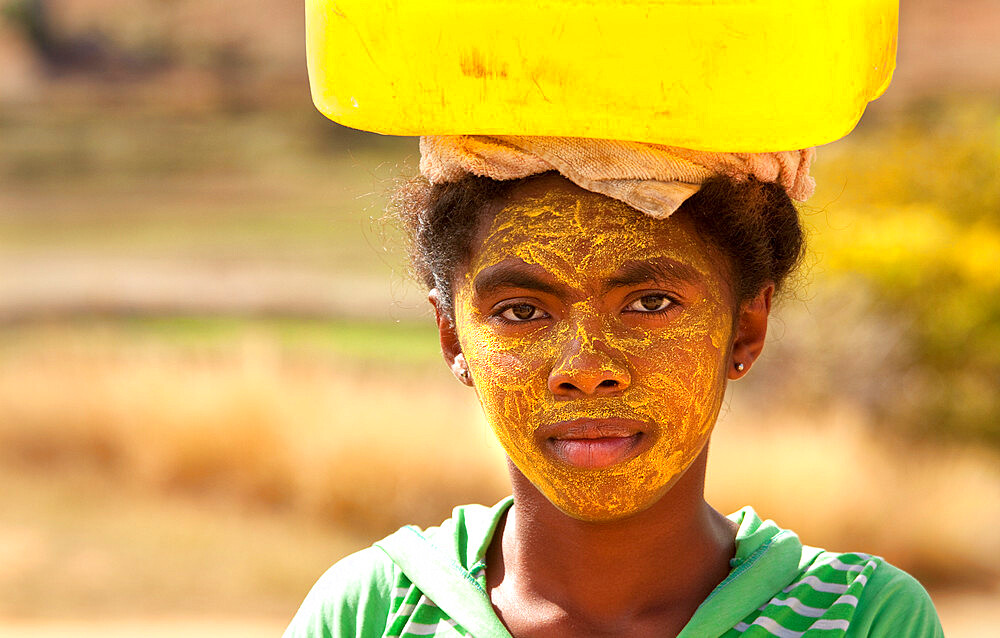 Portrait of woman carrying water, with her face painted to protect the skin from the sun, Isalo, Madagascar, Africa