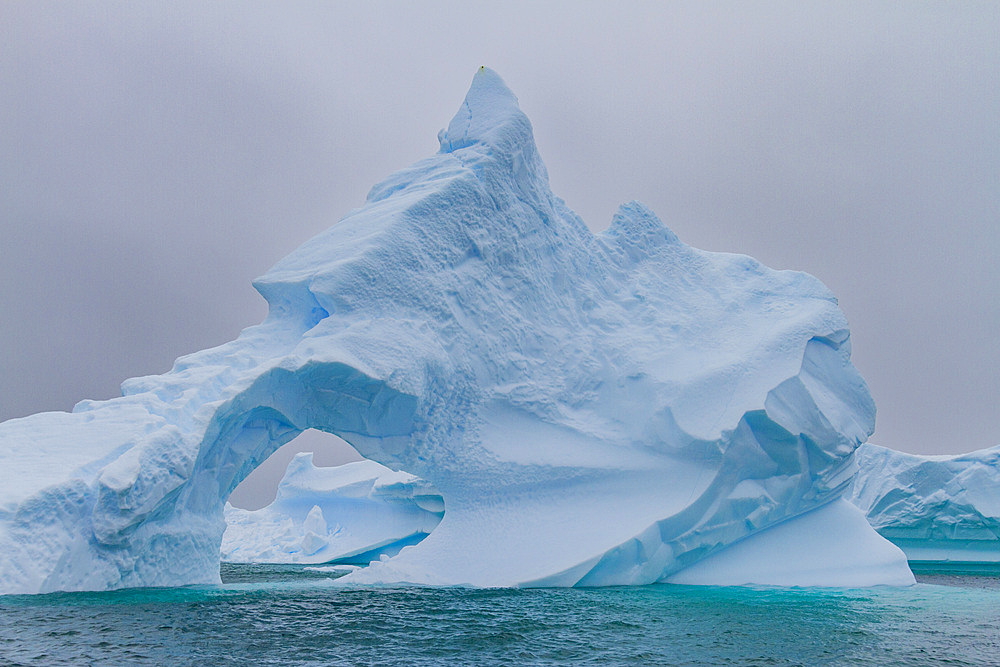 Unusual window formation in iceberg showing Booth Island in the background on the western side of the Antarctic Peninsula.