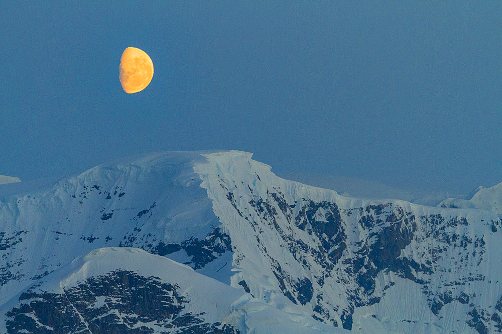 View of the nearly full moon rising over snow-covered mountains on the Antarctic Peninsula, Antarctica, Polar Regions