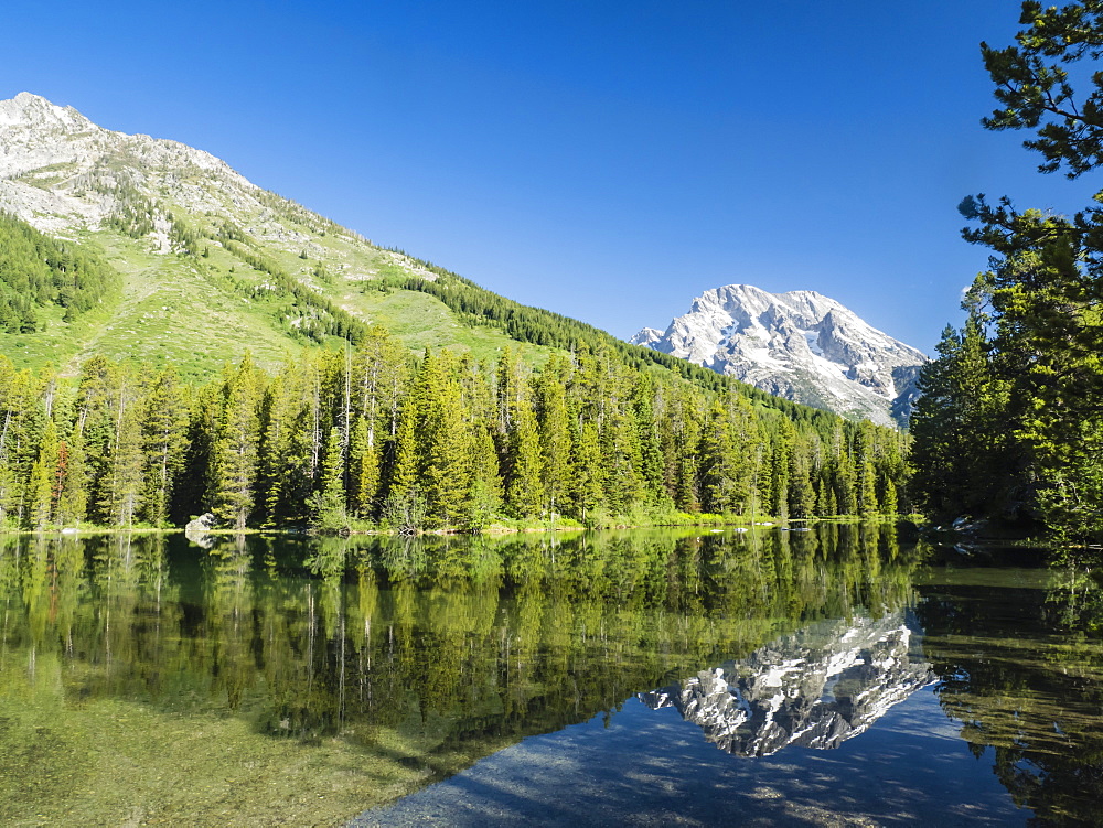 Snow-capped mountains reflected in the calm waters of String Lake, Grand Teton National Park, Wyoming, United States of America, North America