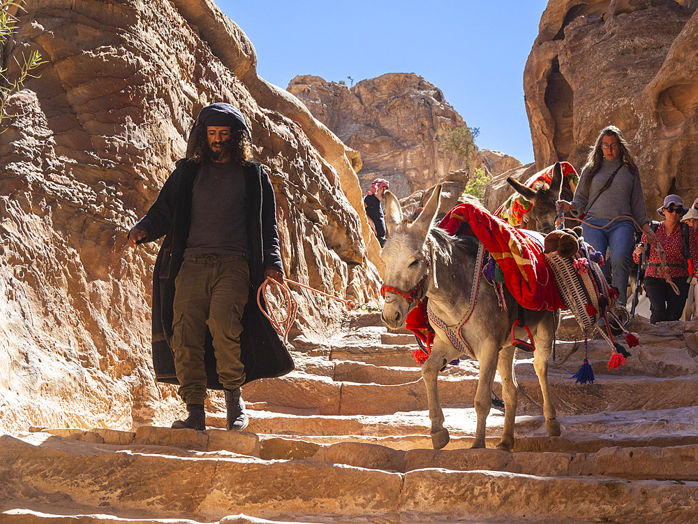 Donkeys, guide and tourists on the path to The Petra Monastery (Al Dayr), Petra Archaeological Park, UNESCO World Heritage Site, one of the New Seven Wonders of the World, Petra, Jordan, Middle East