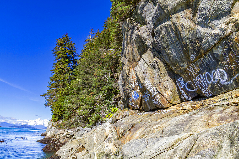 Names of fishing boats painted on the rocks in Cross Sound with the Fairweather Mountain Range as backdrop, Alaska, United States of America, North America