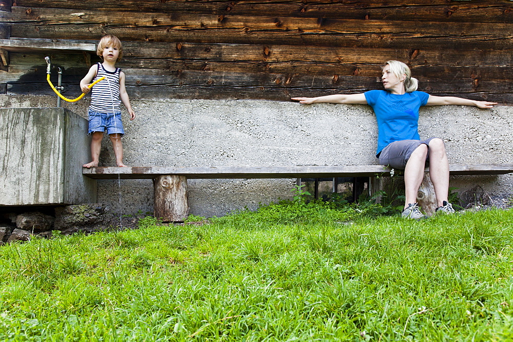 Woman and child on a bench infront of a farmhouse, Kloaschau Valley, Bayrischzell, Bavaria, Germany