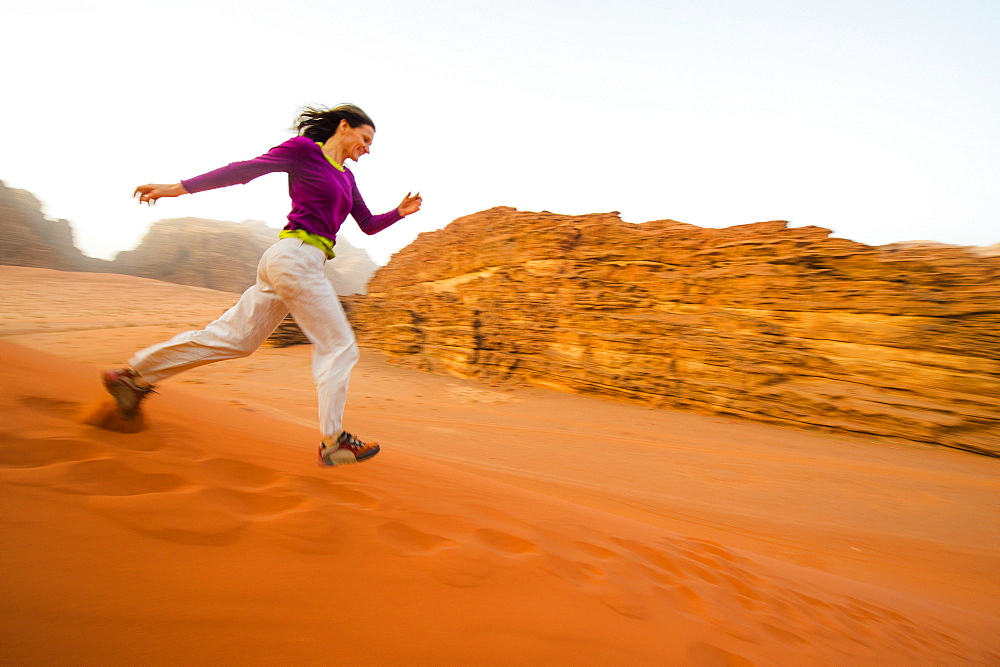 Woman running a sand dune down, Wadi Rum, Jordan, Middle East