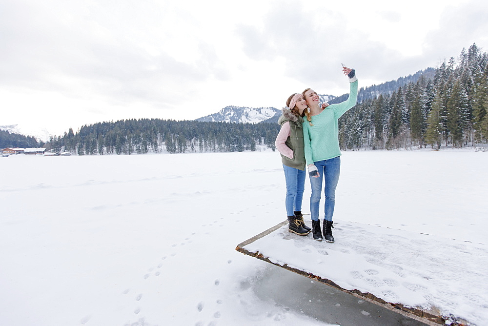 Two young women on jetty photographing themselves, Spitzingsee, Upper Bavaria, Germany