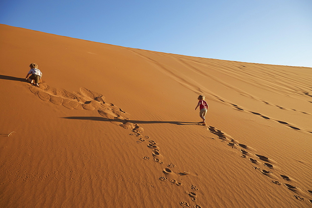 Two boys walking up a sand dune, Deadvlei, Sossusvlei, Namib-Naukluft Park, Namibia