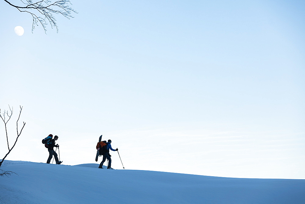 Backcountry snowboarder and snowshoe hikers at dusk in the Tennengebirge mountains, Bischofsmuetze in the background, Salzburg, Austria