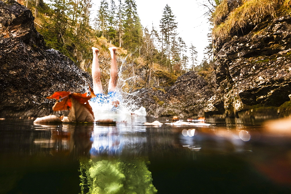 young man jumping from a cliff into mountain stream, Eschenlohe, Upper Bavaria, Germany