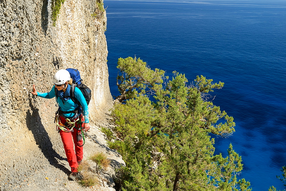 A young woman with trekking gear walking on an exposed ridge in the mountainous coast above the sea, Golfo di Orosei, Selvaggio Blu, Sardinia, Italy, Europe