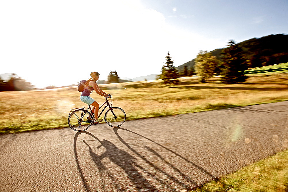 Young woman riding her bike on a sunny day, Tannheimer Tal, Tyrol, Austria