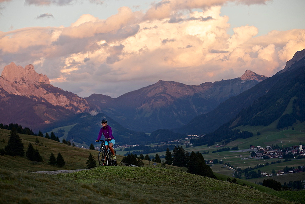 Young woman riding her bike near mountains at sunset, Rote Flueh, Gimpel, Hochwiesler, Tannheimer Tal, Tyrol, Austria