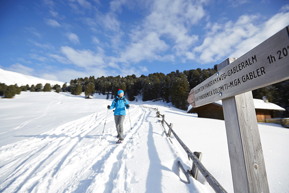 Person snow shoeing in front of signpost, Kreuzwiesenalm, Luesen, South Tyrol, Italy