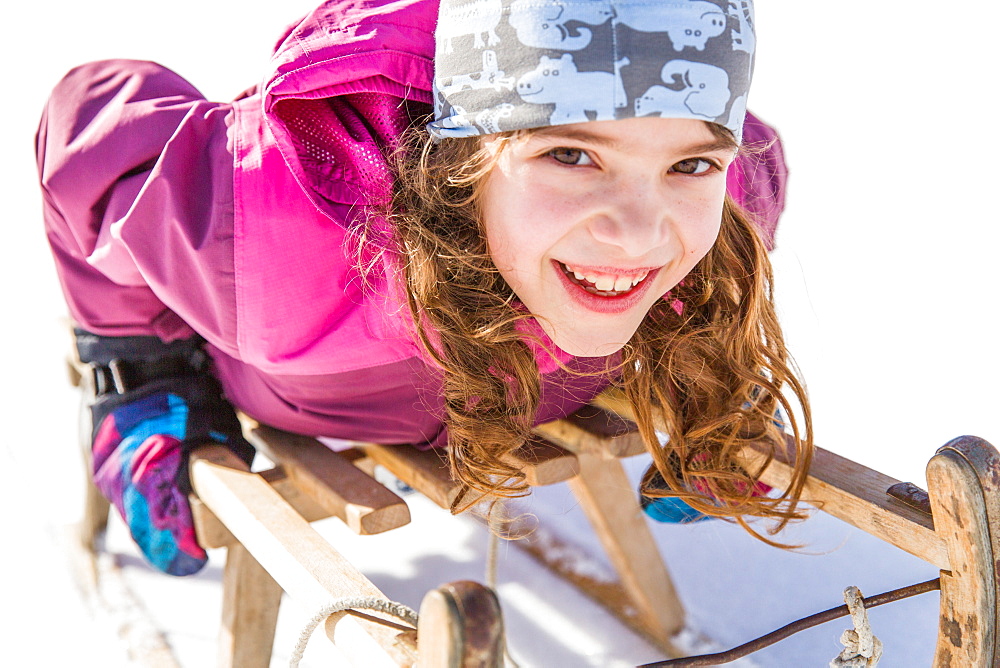 Girl lying on her sledge while sledging, Pfronten, Allgaeu, Bavaria, Germany