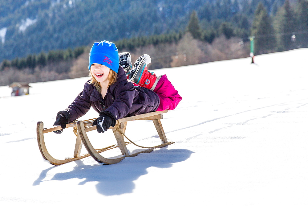 boy lying on his sled while sledging, Pfronten, Allgaeu, Bavaria, Germany