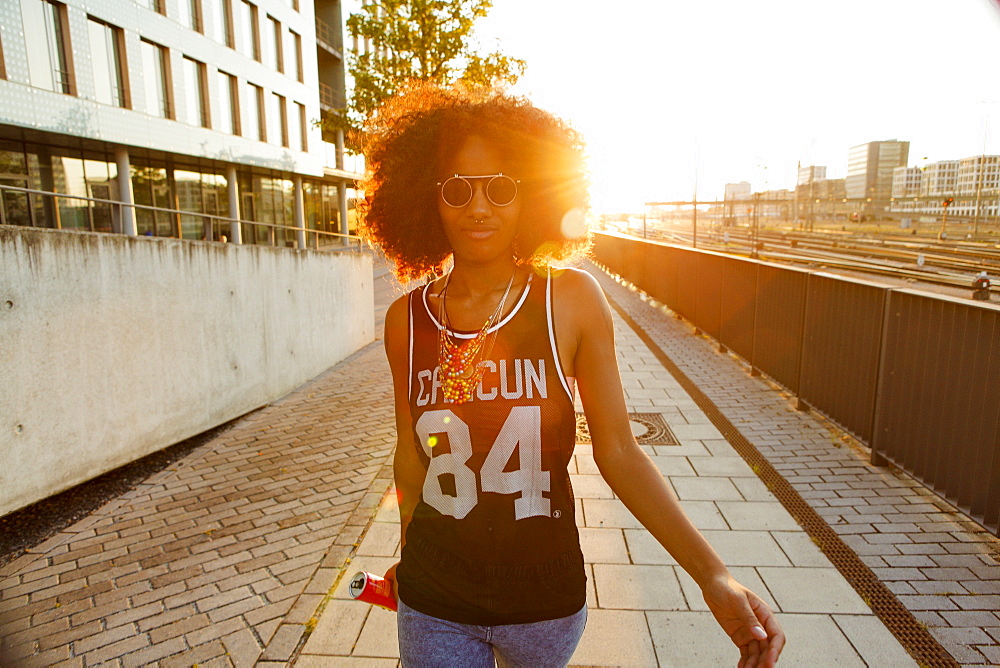 Young sportive and cool afro-american woman with glasses walking in backlight in modern urban scenery , Hackerbruecke, Munich, Bavaria, Germany