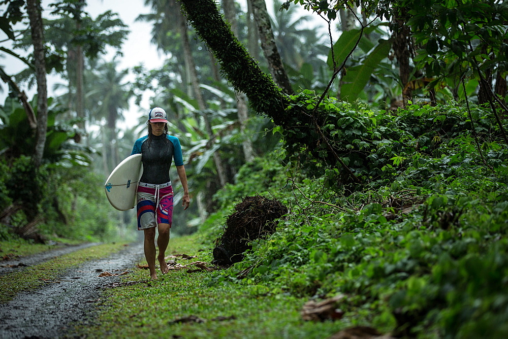 Young female surfer walking on a simple street through a forest, Sao Tome, Sao Tome and Principe, Africa