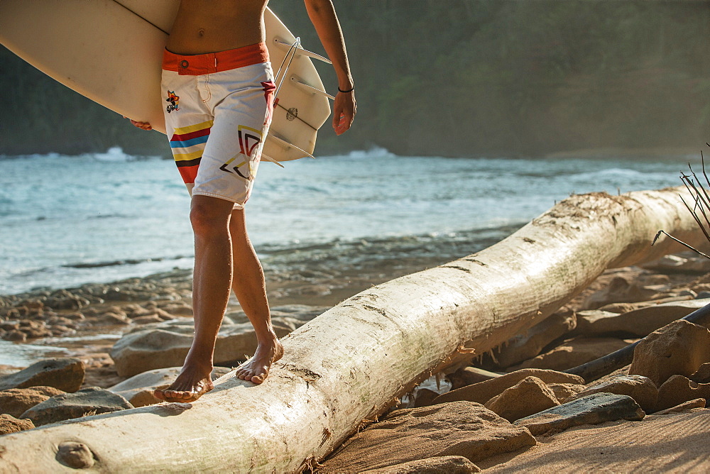 Young female surfer balancing over a trunk on the beach, Sao Tome, Sao Tome and Principe, Africa