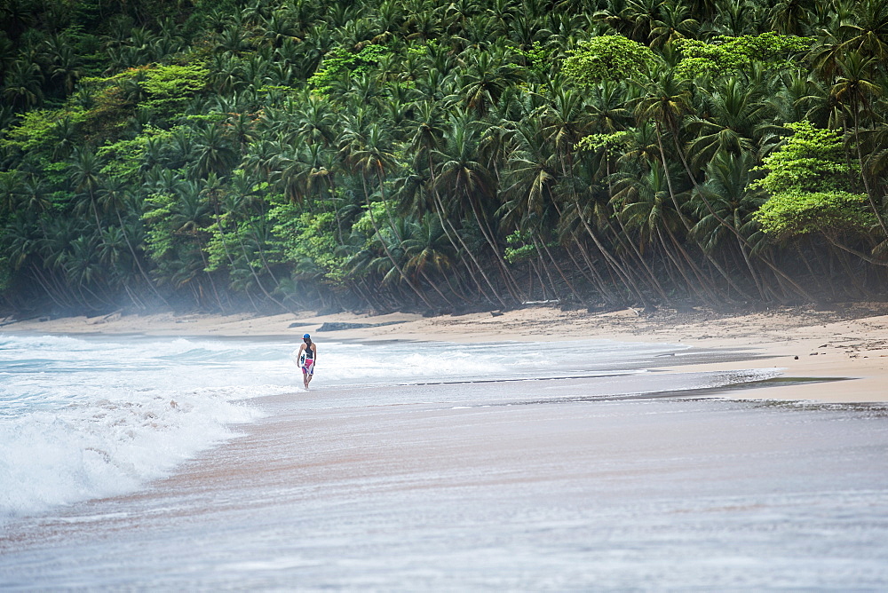 Young female surfer walking along the beach, Sao Tome, Sao Tome and Principe, Africa