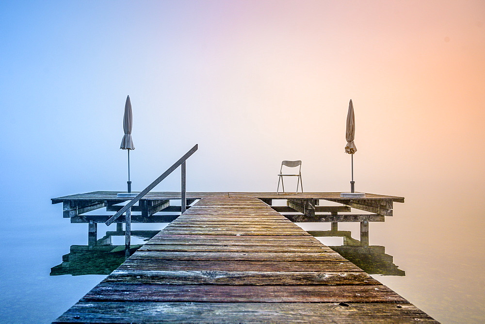 Jetty with folded parasols at misty sunrise on Lake Starnberg, Seeshaupt, Bavaria, Germany