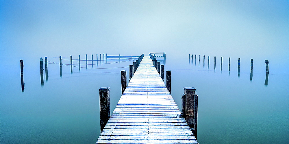 Snow-covered jetty in marina at misty sunrise on Lake Starnberg, Seeshaupt, Bavaria, Germany