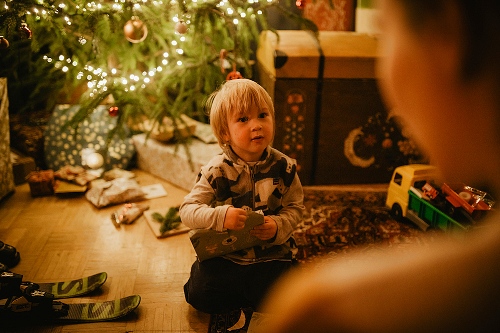 little boy unwraps his gifts in front of the Christmas tree, Christmas, family