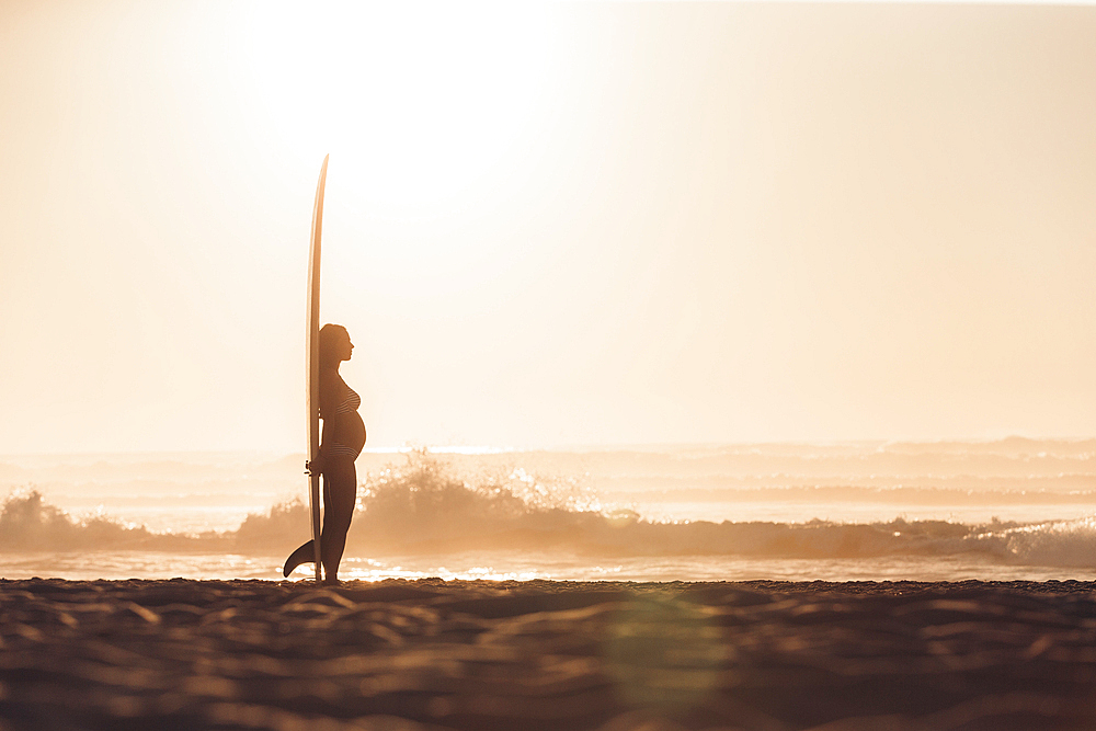 pregnant woman standing with surfboard on the beach, surfing, pregnancy, Portugal