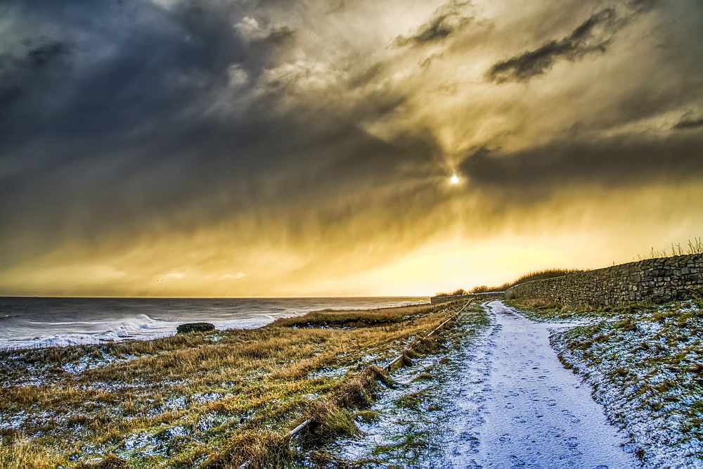 Snow-covered path along the coastline with golden sunlight illuminating the clouds, South Shields, Tyne and Wear, England