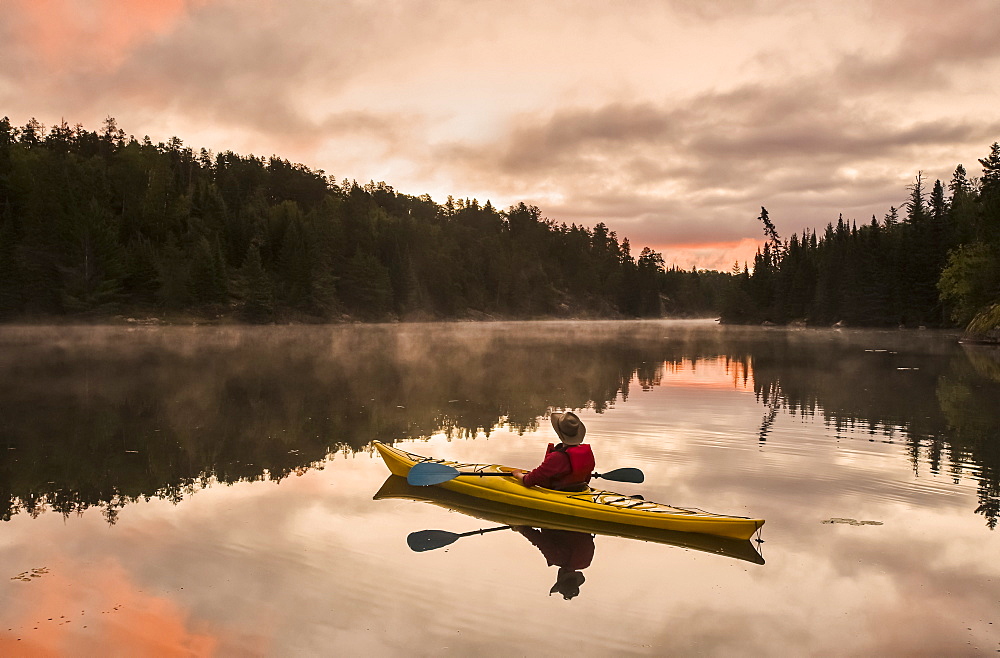 A man kayaking at sunset in the Rushing River, near Kenora, Ontario, Canada