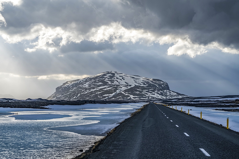 Road leading into the dramatic landscape of Iceland while the sun shines through the clouds making a beautiful scene, Iceland