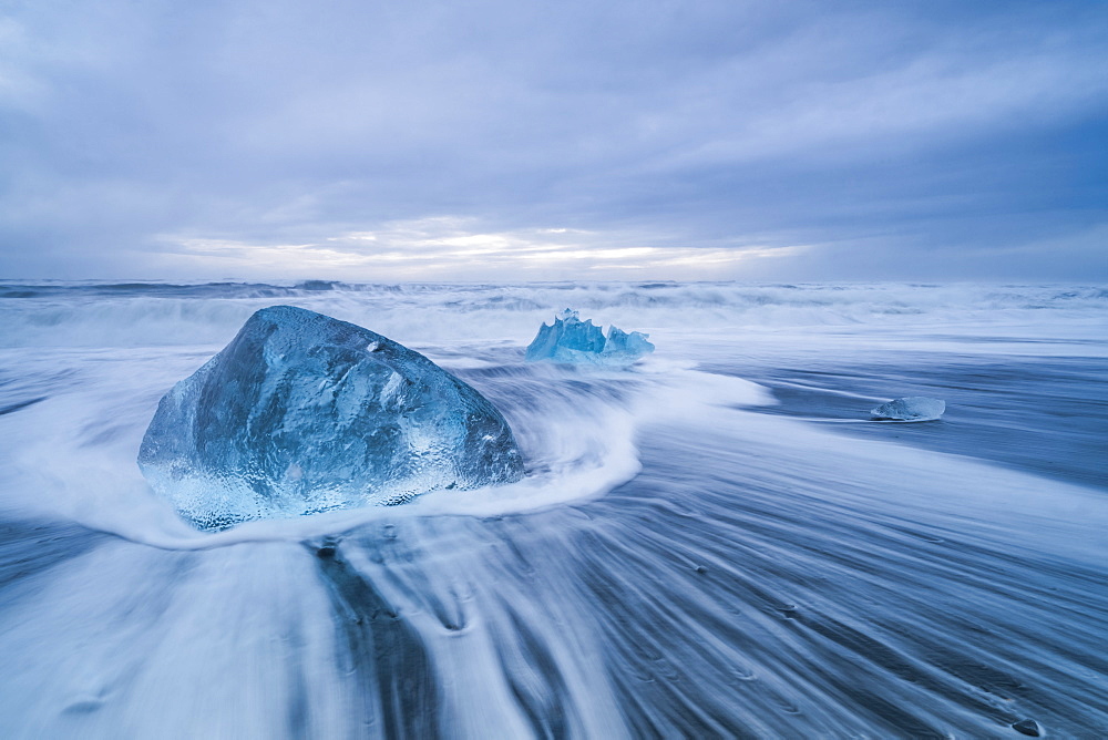 Large ice block laying on the shores of Southern Iceland while waves crash on shore, Iceland