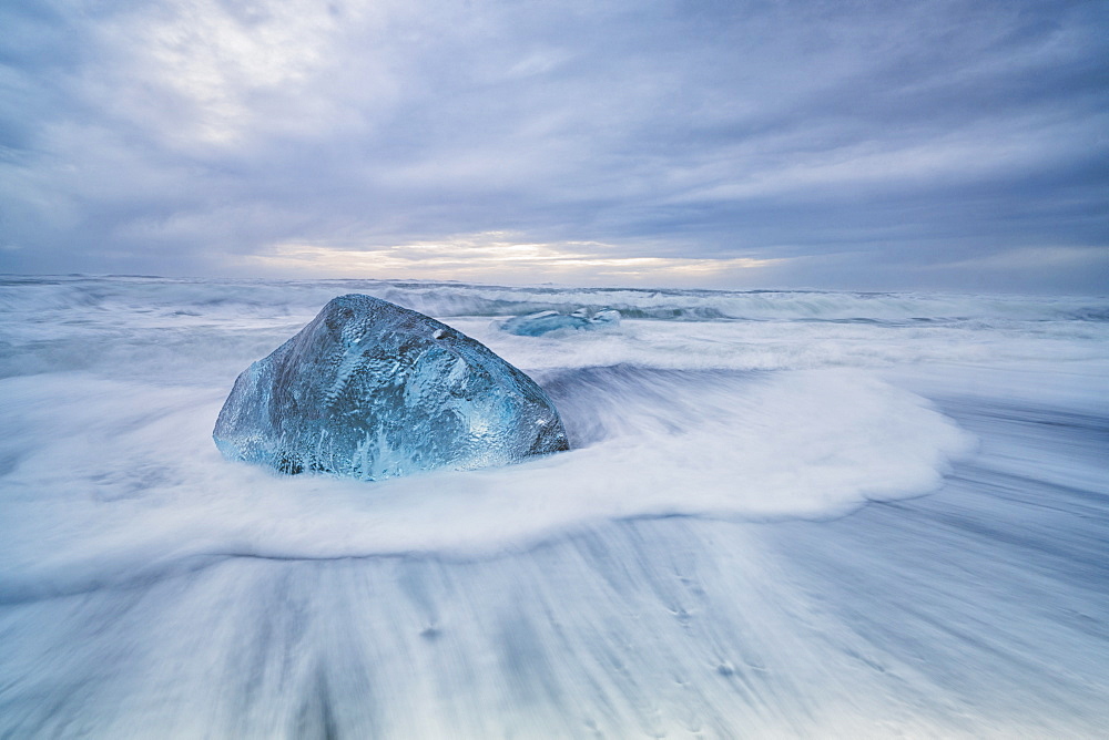 Large ice block laying on the shores of Southern Iceland while waves crash on shore, Iceland