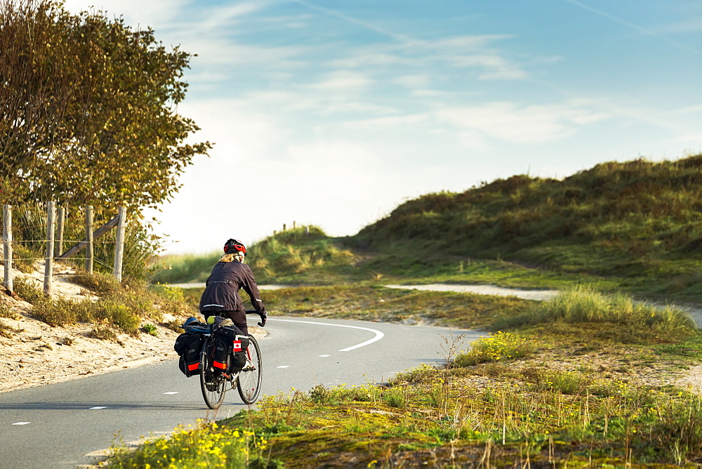 Female cyclist on paved bike pathway along rolling sand dunes and grassy hills, South of Zandvoort, Netherlands