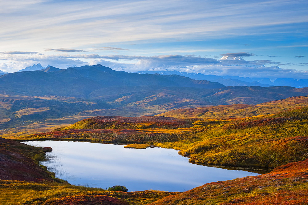 A view from Peters Hills of the setting sun with parting clouds revealing 20,320' Mount McKinley with a unnamed lake in the foreground, Alaska, United States of America