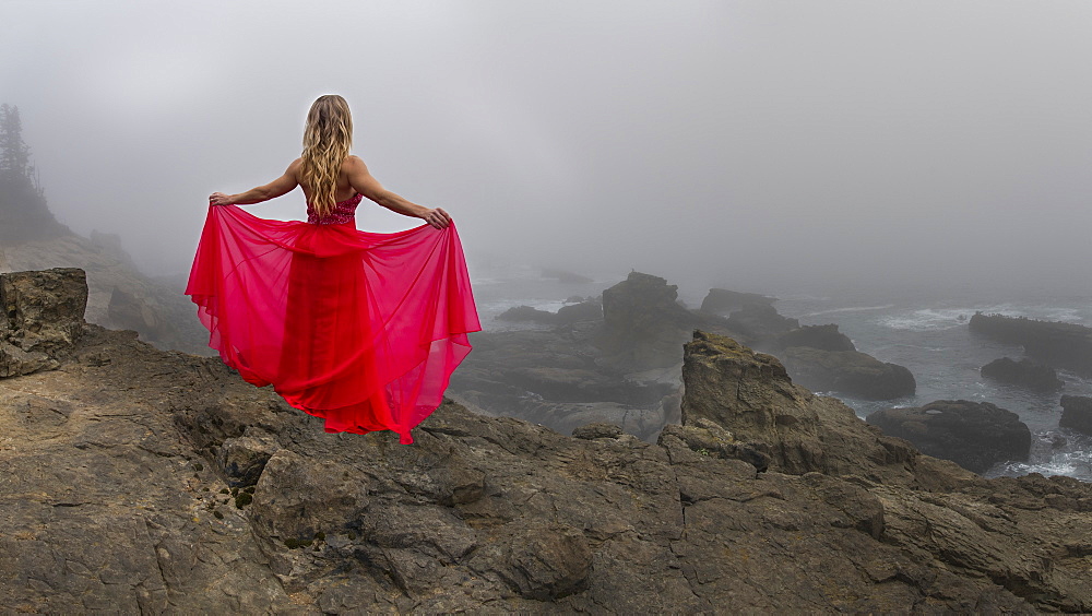 A woman stands on a cliff edge overlooking the angry sea on a foggy late afternoon in State Arago Park, stitched pano composite, Coos County, Oregon, United States of America