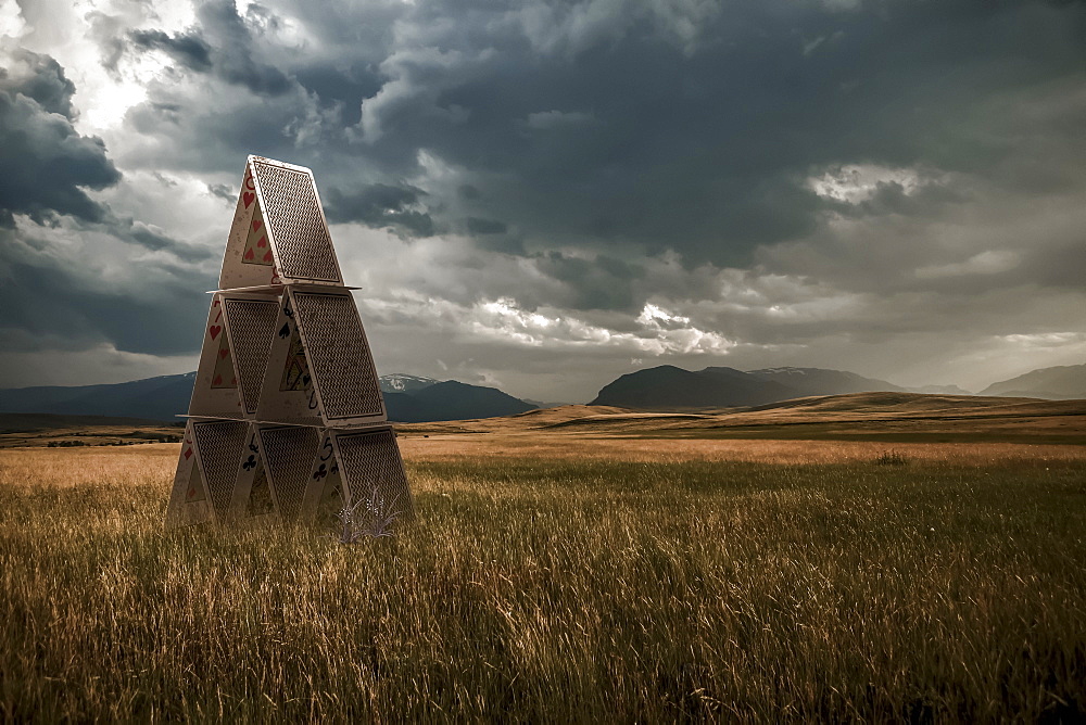 Playing cards set up in a grass field under a stormy sky, composite image