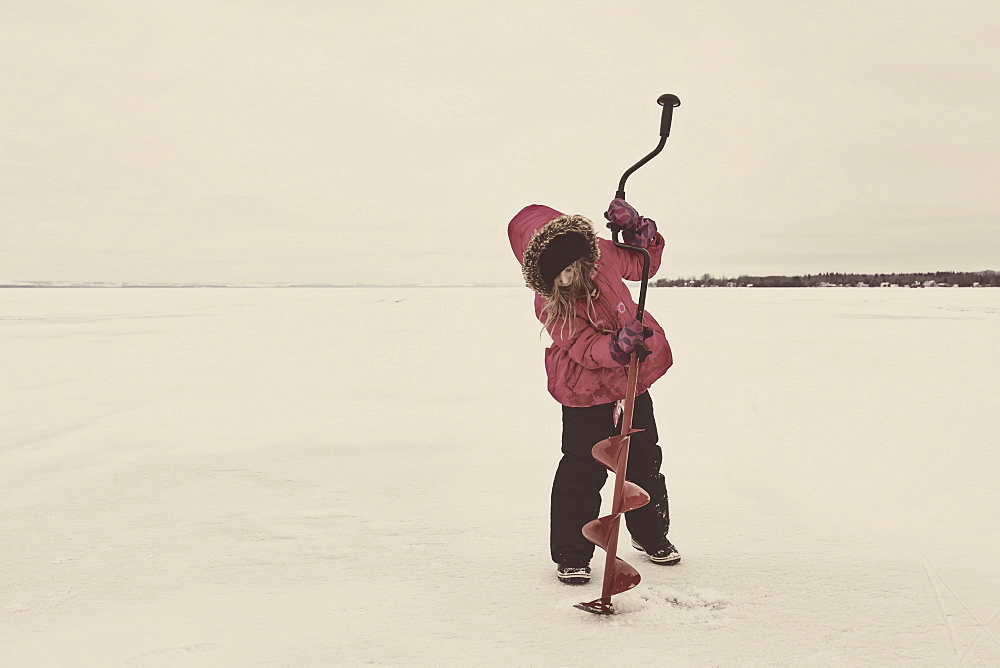 Young Girl Trying To Drill A Hole In The Ice Of Frozen Lake Wabamun Without Any Success: Wabamun, Alberta, Canada