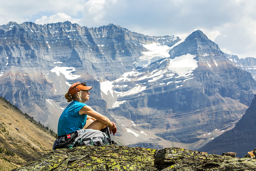 Female hiker sitting on a rocky area overlooking mountain vista in the background, British Columbia, Canada